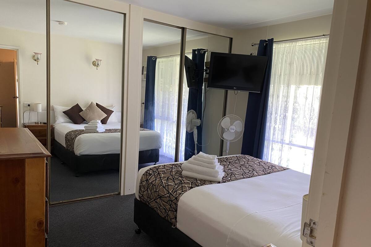 A hotel room with two beds, a TV, a mirror, and a desk.