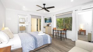 A modern bedroom with a bed, a ceiling fan, a dining area with a table and chairs, and a view of the outdoors. - Tiarri Terrigal (Terrigal)