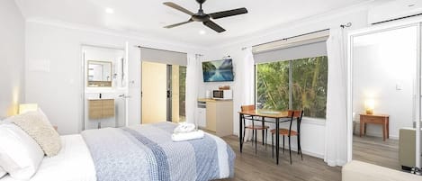 A modern bedroom with a bed, a ceiling fan, a dining area with a table and chairs, and a view of the outdoors.