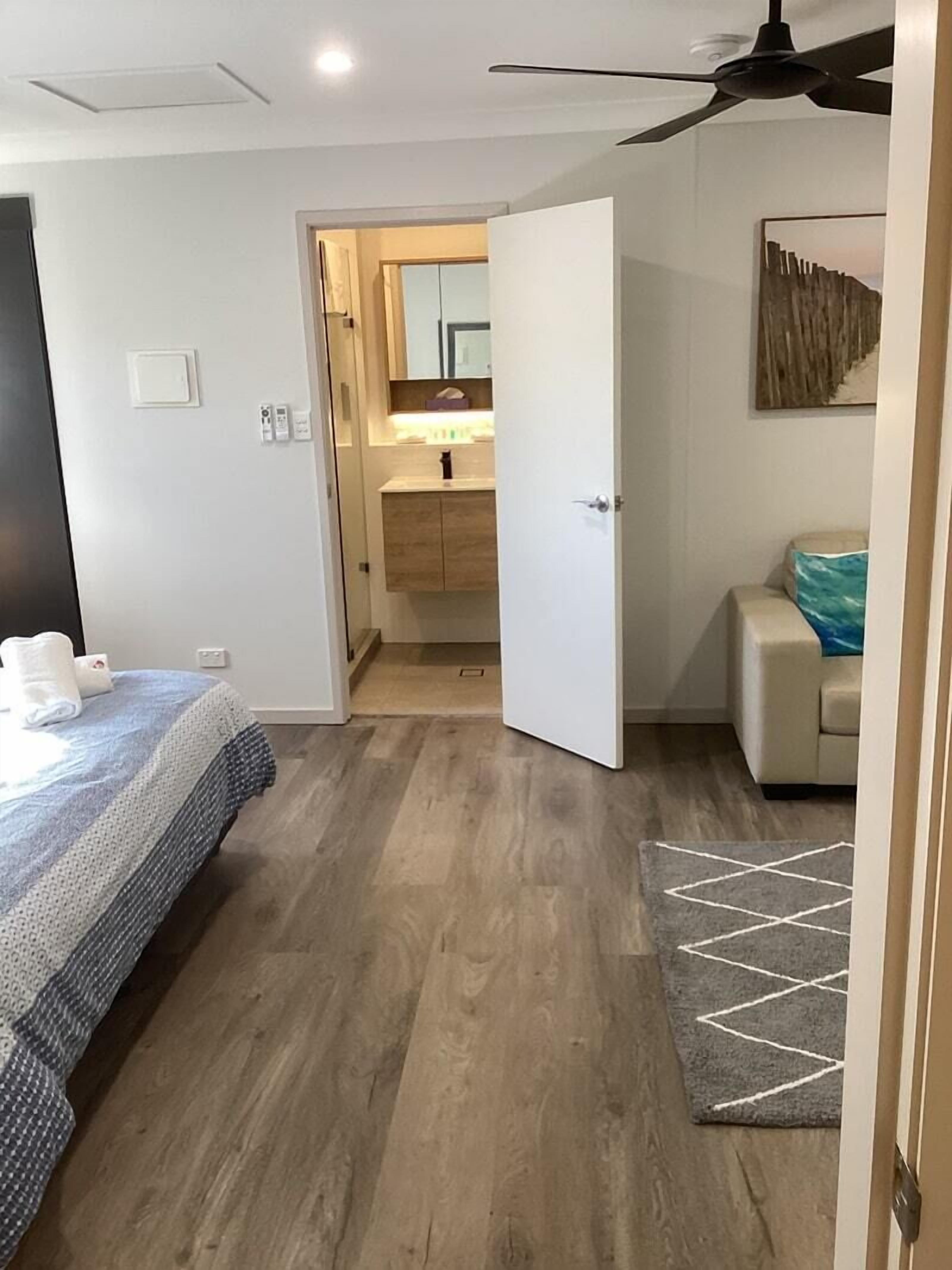 A hotel room with a bed, a small bathroom, a ceiling fan, and a rug.