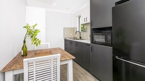 A modern kitchen with dark cabinetry, a stainless steel refrigerator, and a microwave. - Tiarri Terrigal (Terrigal)