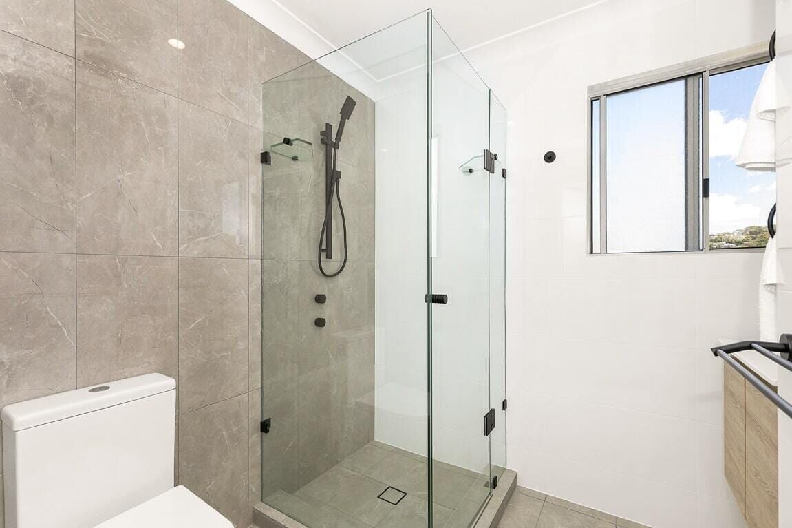 Un baño moderno con ducha de vidrio, inodoro y ventana con vistas.