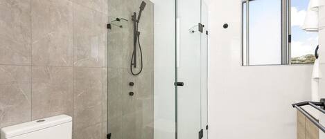 Un baño moderno con ducha de vidrio, inodoro y ventana con vistas.