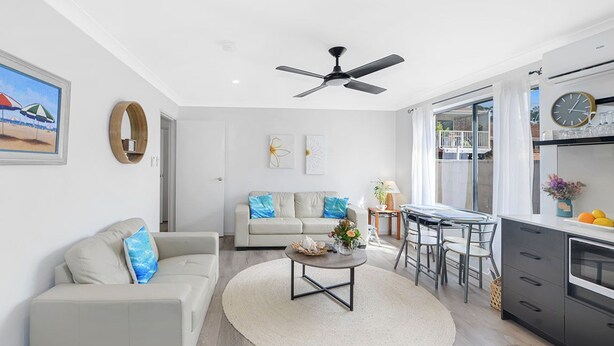 A modern living room with a sofa, coffee table, and dining area. - Tiarri Terrigal (Terrigal)
