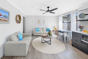 A modern living room with a sofa, coffee table, and dining area. - Tiarri Terrigal (Terrigal)