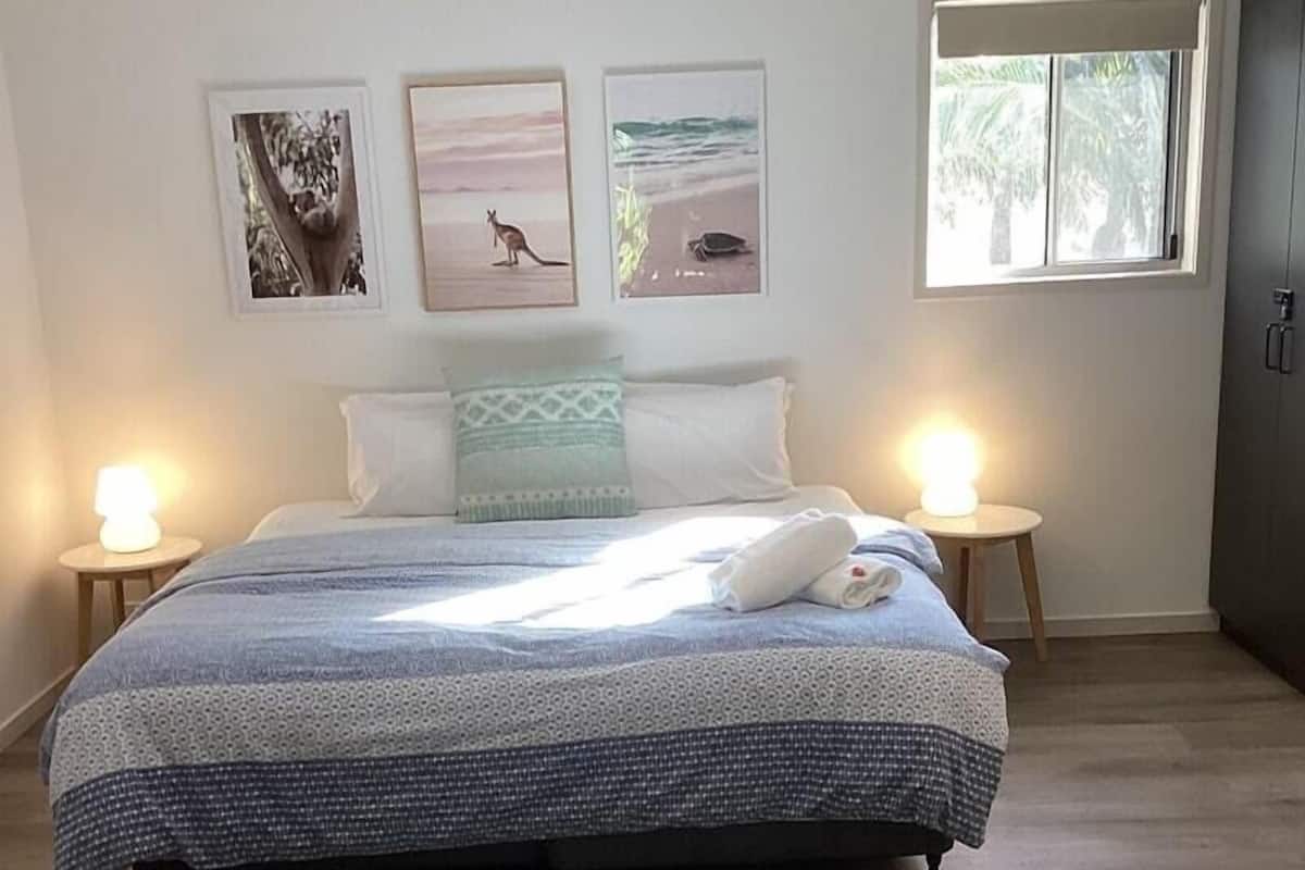 Un dormitorio con una cama, dos lámparas de noche, un ventanal y tres cuadros en la pared.
