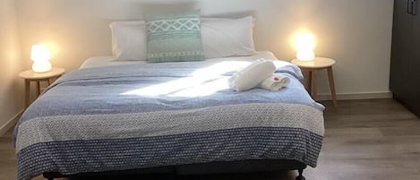 A bedroom with a bed, two bedside lamps, a window, and three framed pictures on the wall.
