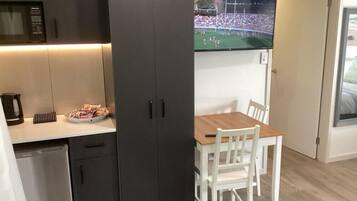 Eine kleine Küche mit dunklen Schränken, einem Holztisch und einem darüber montierten Fernseher.