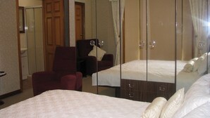 Habitación de hotel con un espejo grande, una cama con ropa de cama blanca, un sillón rojo y un armario de madera.