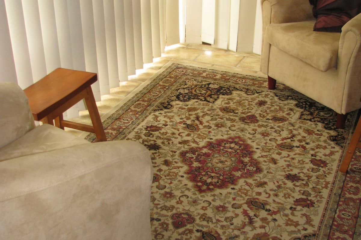 A living room with a beige armchair, a wooden side table, and a patterned rug.