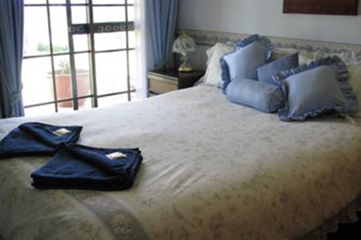 A neatly made bed with pillows, a bedside table with a lamp, and a window with curtains.