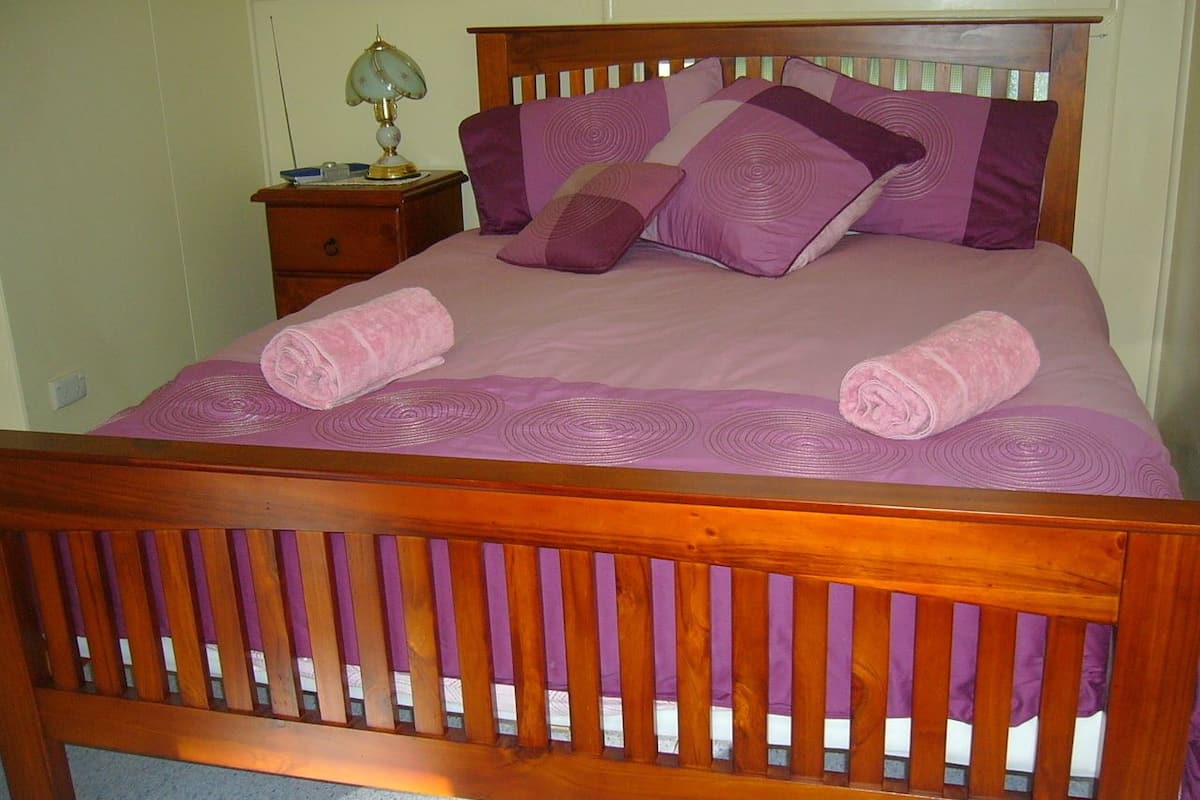 Un lit en bois avec une tête de lit, une table de chevet avec une lampe et deux serviettes enroulées posées sur le lit.