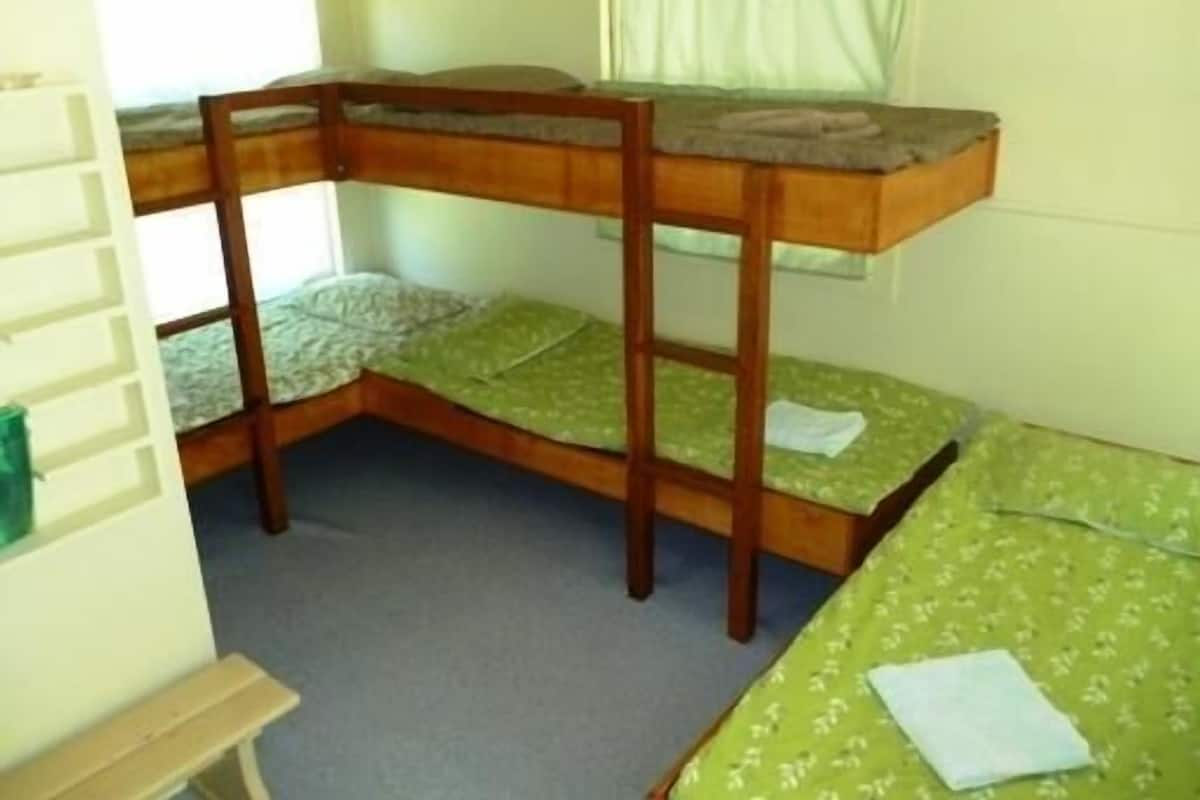 Une chambre avec un lit superposé, deux lits, un petit banc et une fenêtre avec des rideaux.