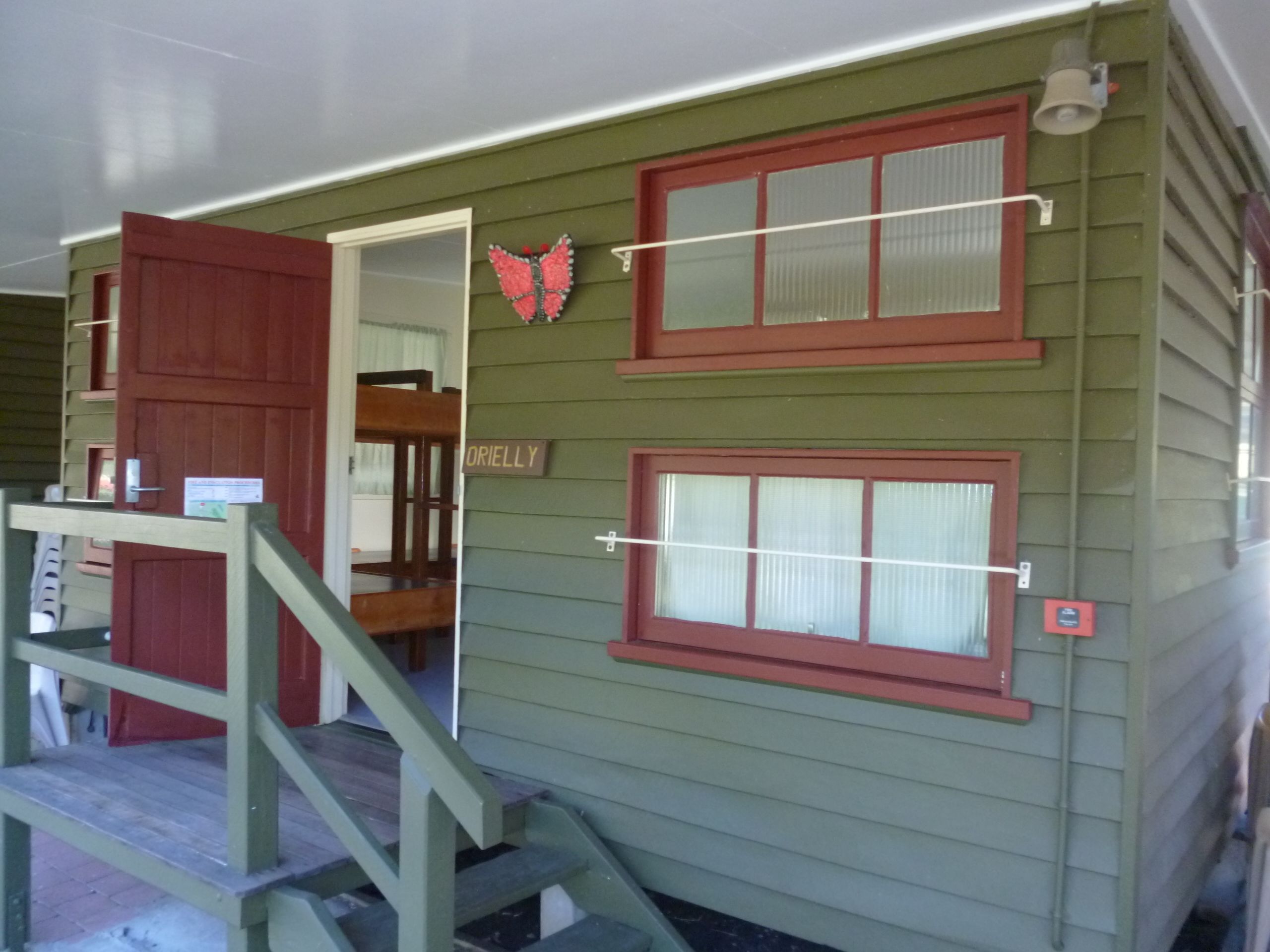 A small, single-story building with a green exterior and red-framed windows. A wooden staircase leads to a door labeled "ORIELLY."