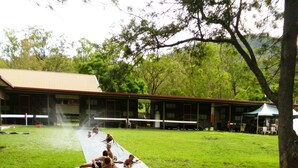 Un groupe de personnes est allongé sur un tapis noir dans un espace herbeux, avec des arbres et un bâtiment en arrière-plan.