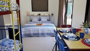 Une chambre de dortoir avec des lits superposés, un lit simple, une table à manger avec des chaises et une fenêtre avec des rideaux.