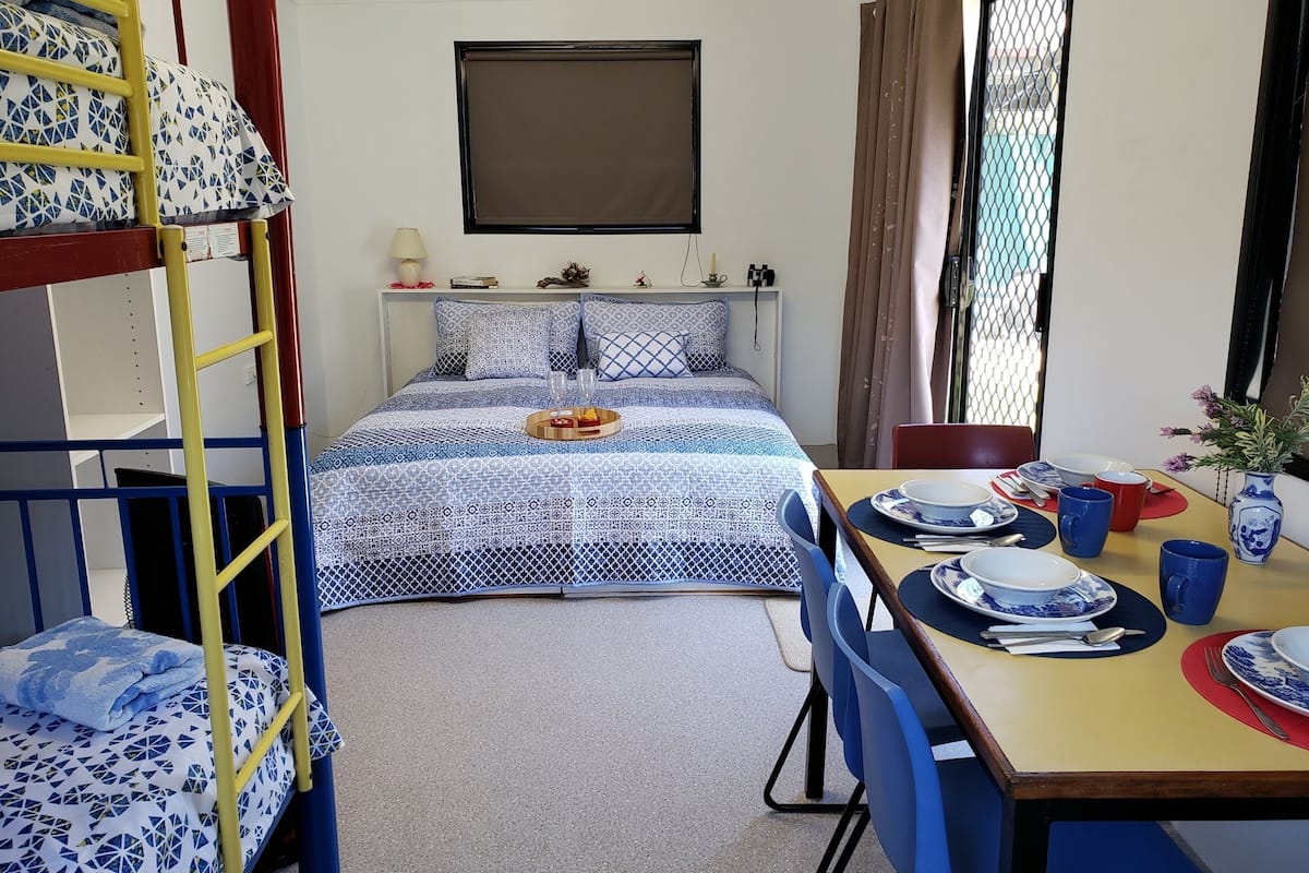 Une chambre de dortoir avec des lits superposés, un lit simple, une table à manger avec des chaises et une fenêtre avec des rideaux.