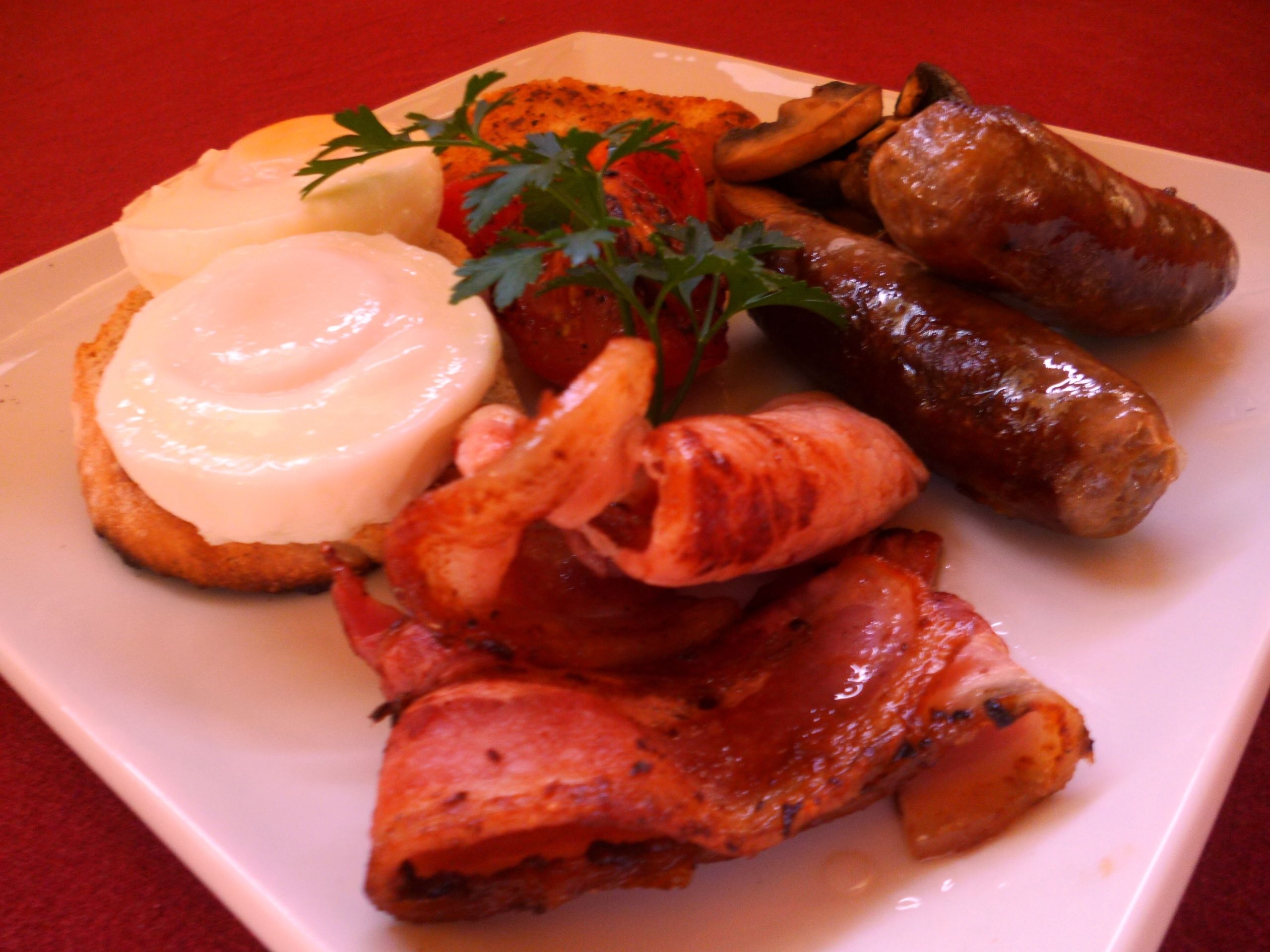 A plate of food including sausages, bacon, and a poached egg with hollandaise sauce.