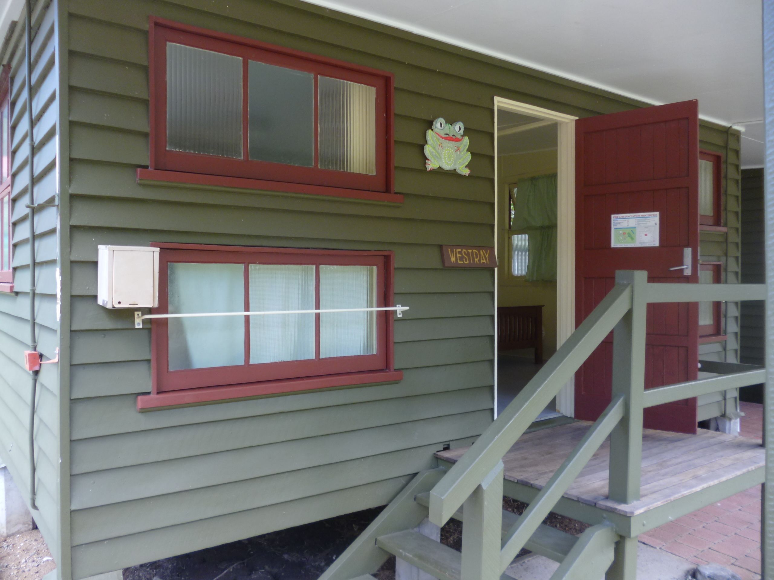 A green building with two windows, a wooden staircase, and a door labeled "WESTTRAY".