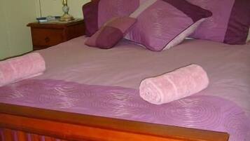 A bed with a wooden frame, purple bedding, and a rolled towel on it.