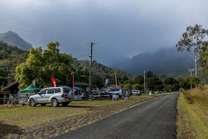 A rural road with parked cars and a green tent, surrounded by trees and mountains. - Christmas Creek Cafe & Cabins (Lamington)