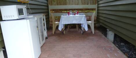 A patio area with a table set for dining, a refrigerator, and a microwave.