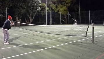 Ein Tennisplatz im Freien mit Netz in der Mitte, umgeben von einem Zaun und Bäumen im Hintergrund.