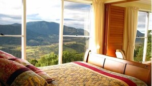 Un dormitorio con una cama grande, un cabecero de madera y vistas a montañas a través de amplios ventanales.