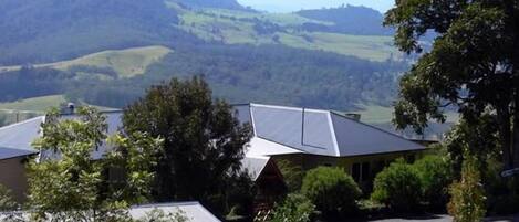 A building with a sloped roof, surrounded by greenery and hills in the background.