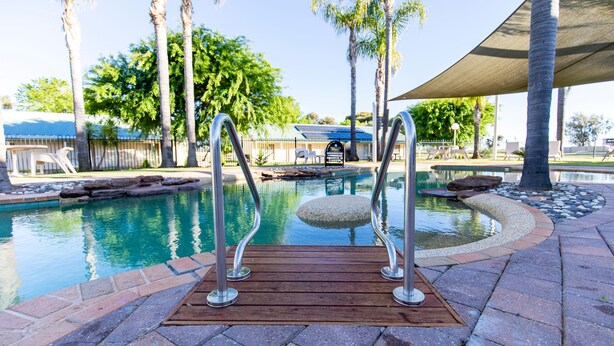 A pool with a wooden deck and metal railings, surrounded by palm trees and a covered seating area. - Murray Downs Resort (Murray Downs)