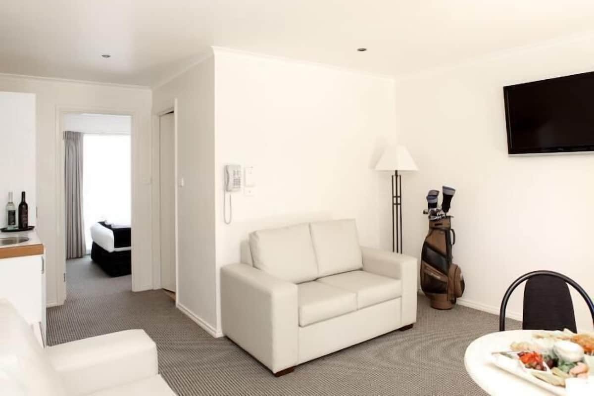 A hotel room with a white sofa, a dining table with a plate of food, a lamp, and a guitar.