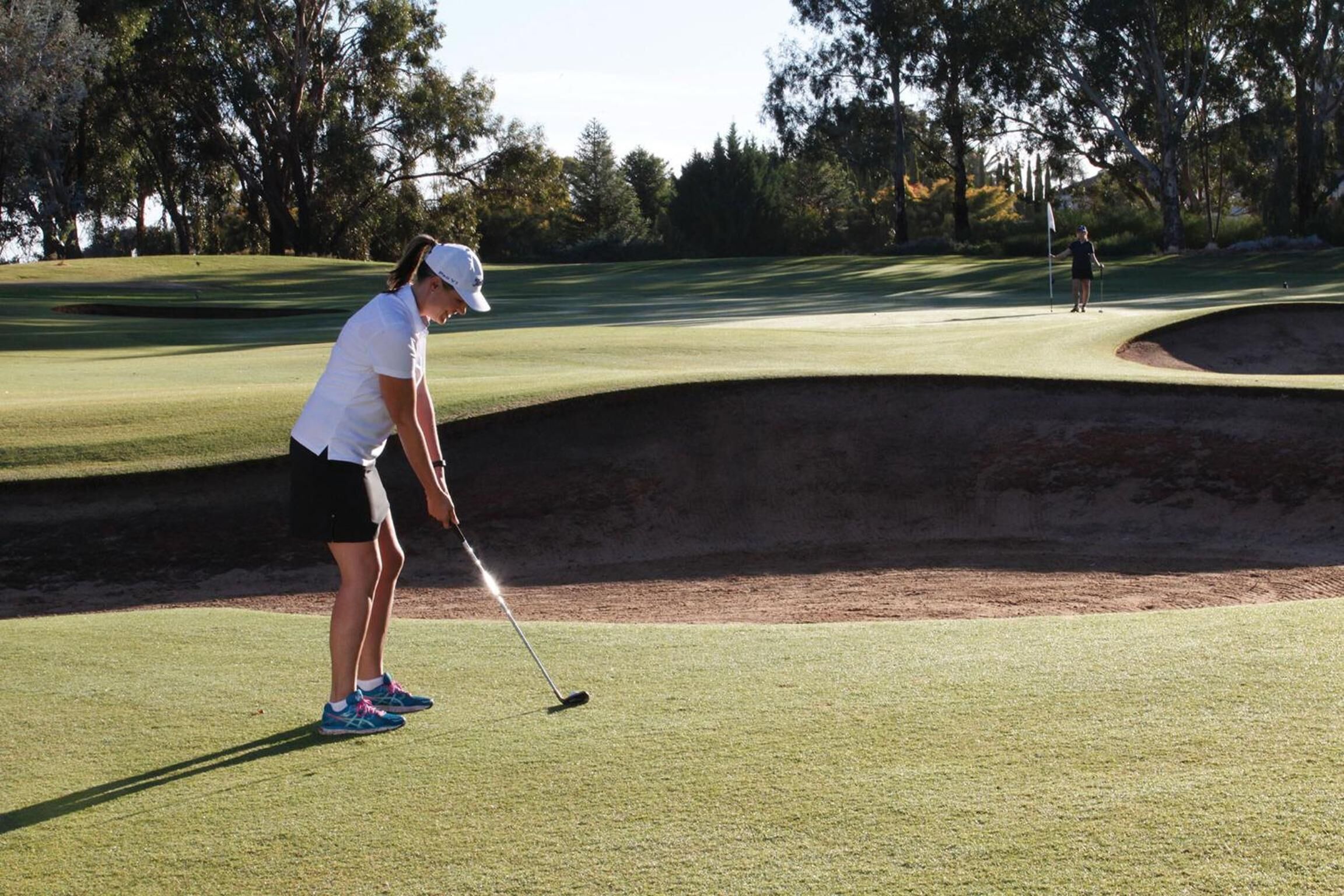 Una persona jugando al golf en un campo bien cuidado, con árboles de fondo.