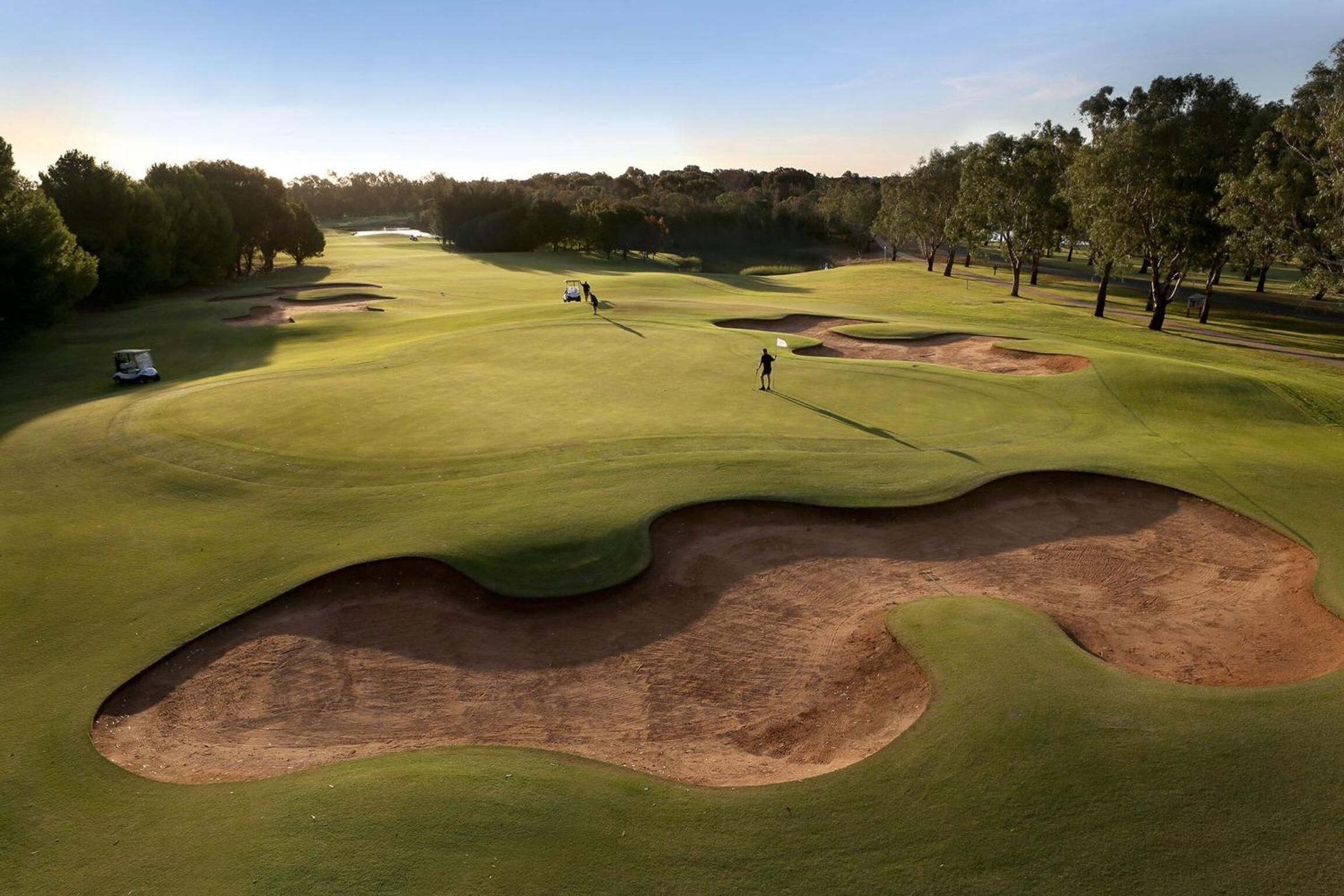 Un campo de golf con búnkeres, árboles y cielo despejado.