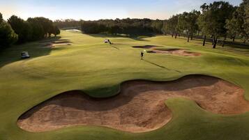 Un campo de golf con búnkeres, árboles y cielo despejado.