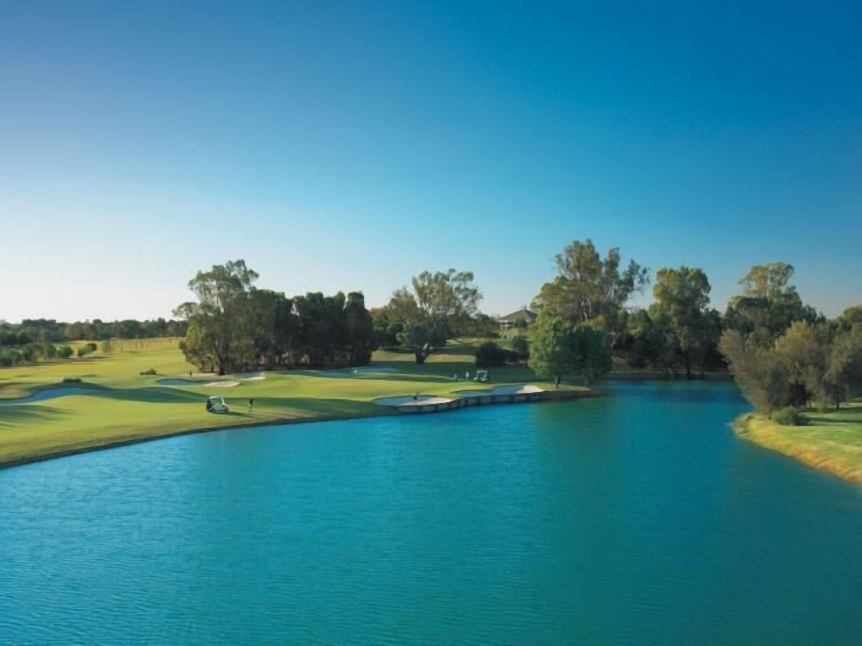 A golf course with a water body and trees.