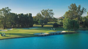 A golf course with a water hazard, trees, and a clubhouse. - Murray Downs Resort (Murray Downs)