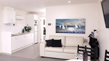 A modern kitchen with white cabinets, a dining area with a white sofa, and a painting of sailboats on the wall.