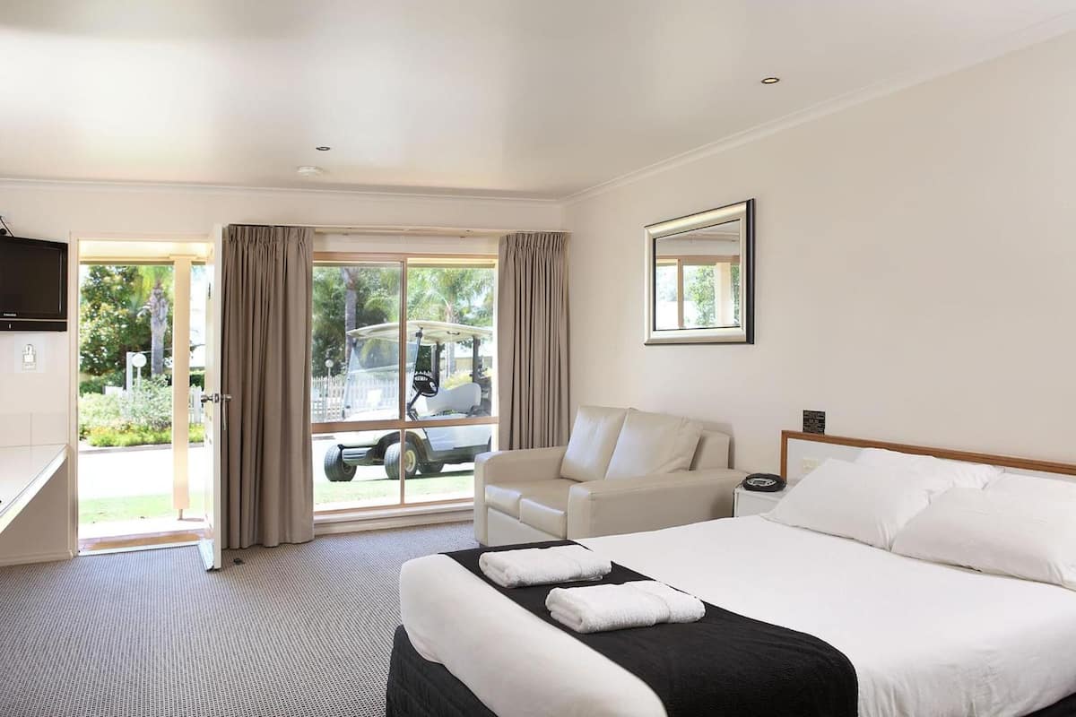 A hotel room with a bed, a sofa, a TV, and a window with curtains.