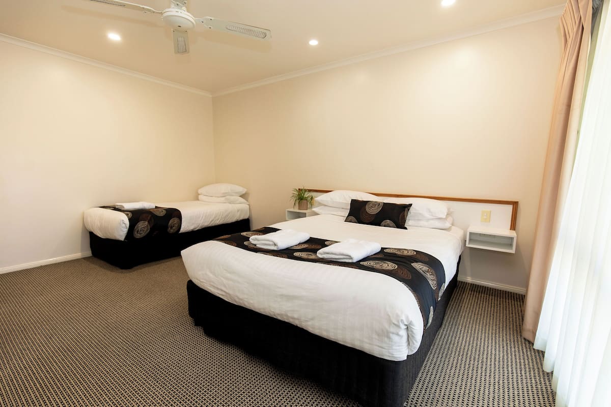 A hotel room with two beds, a ceiling fan, and a small bedside table.