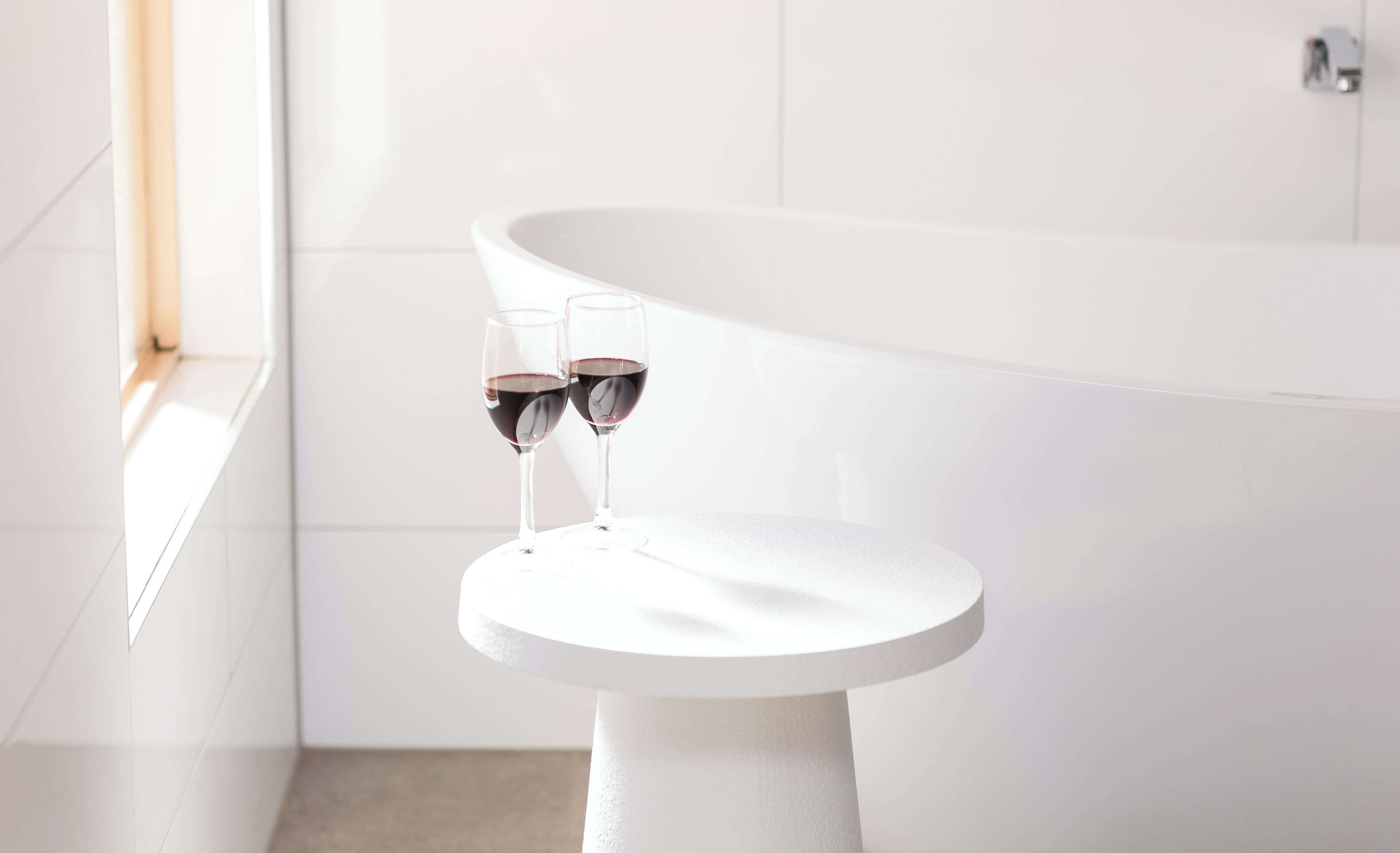 Una bañera blanca con dos copas de vino tinto sobre una mesita blanca.