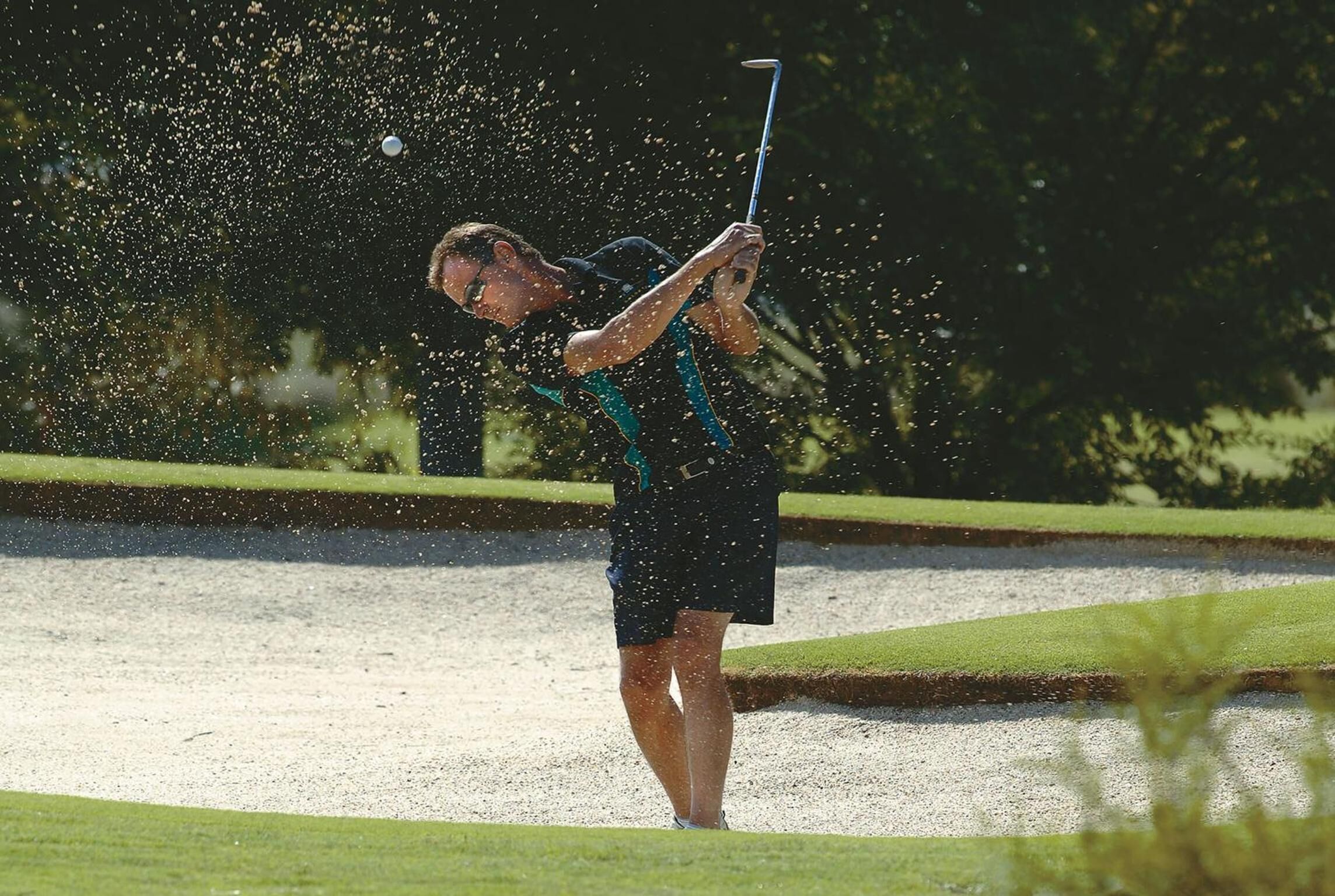 Una persona jugando al golf en un campo con búnkeres de arena y césped verde.