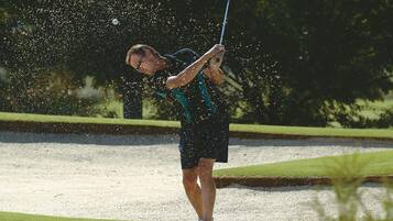Una persona jugando al golf en un campo con búnkeres de arena y césped verde.
