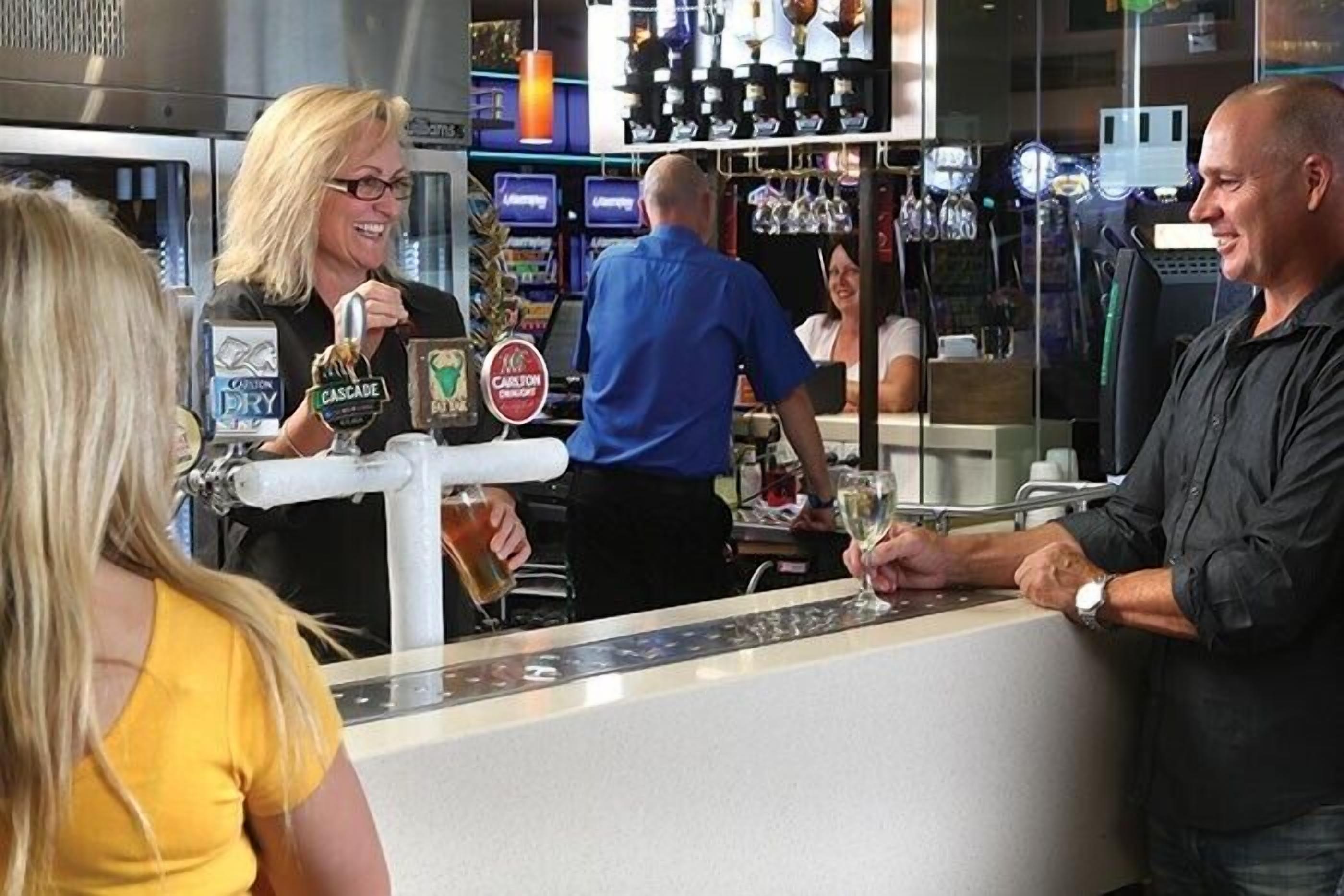 A bar area with a counter, a person pouring a drink, and a shelf with bottles.