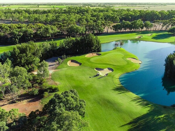 A golf course with a pond, surrounded by dense trees and open fields.