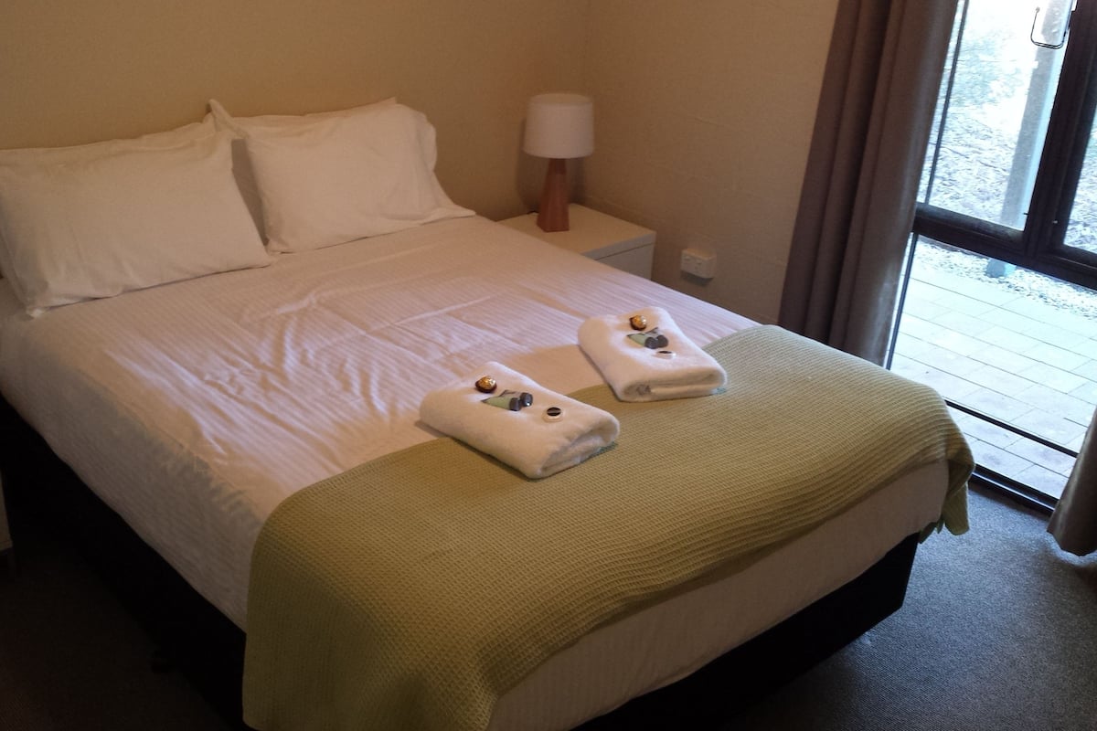 A hotel room with a bed, two bedside tables, a lamp, and a window.