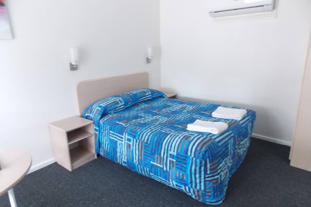 Un dormitorio pequeño y ordenado con una cama individual, una mesita de noche y un aire acondicionado de pared.