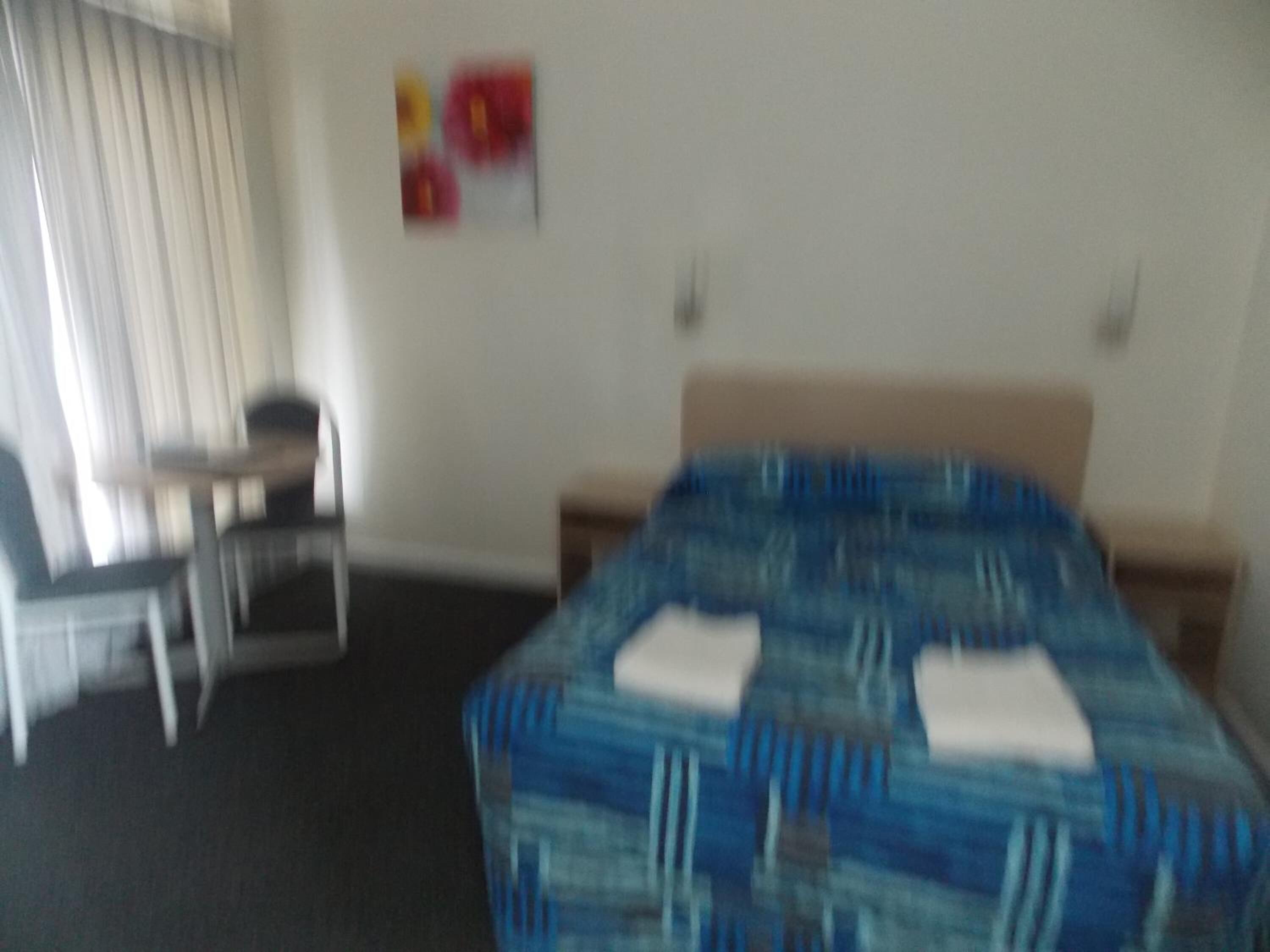 A hotel room with a bed, a chair, a desk, and a wall with a picture.