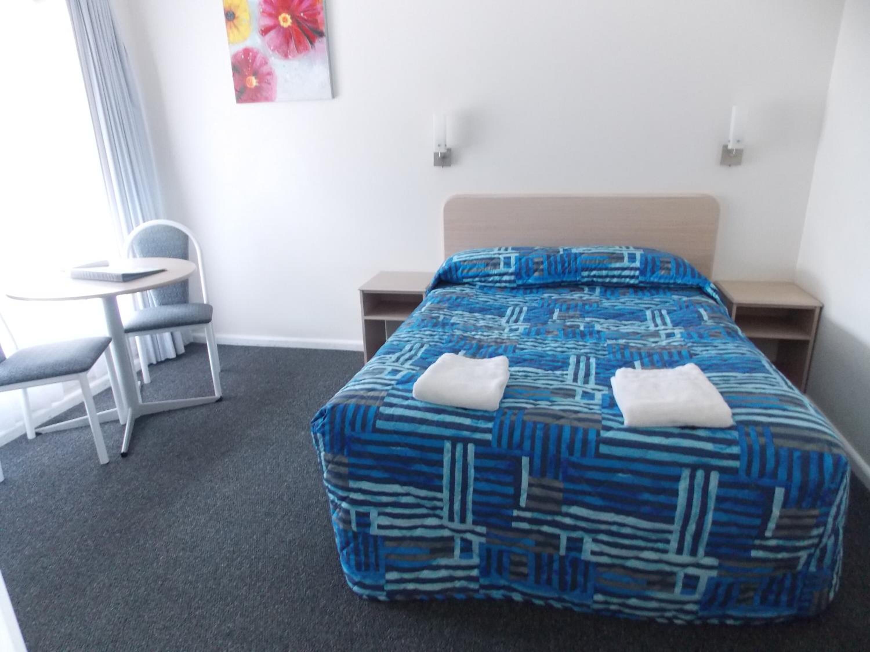Una habitación de hotel con una cama, dos mesitas de noche, una silla y una pequeña mesa.