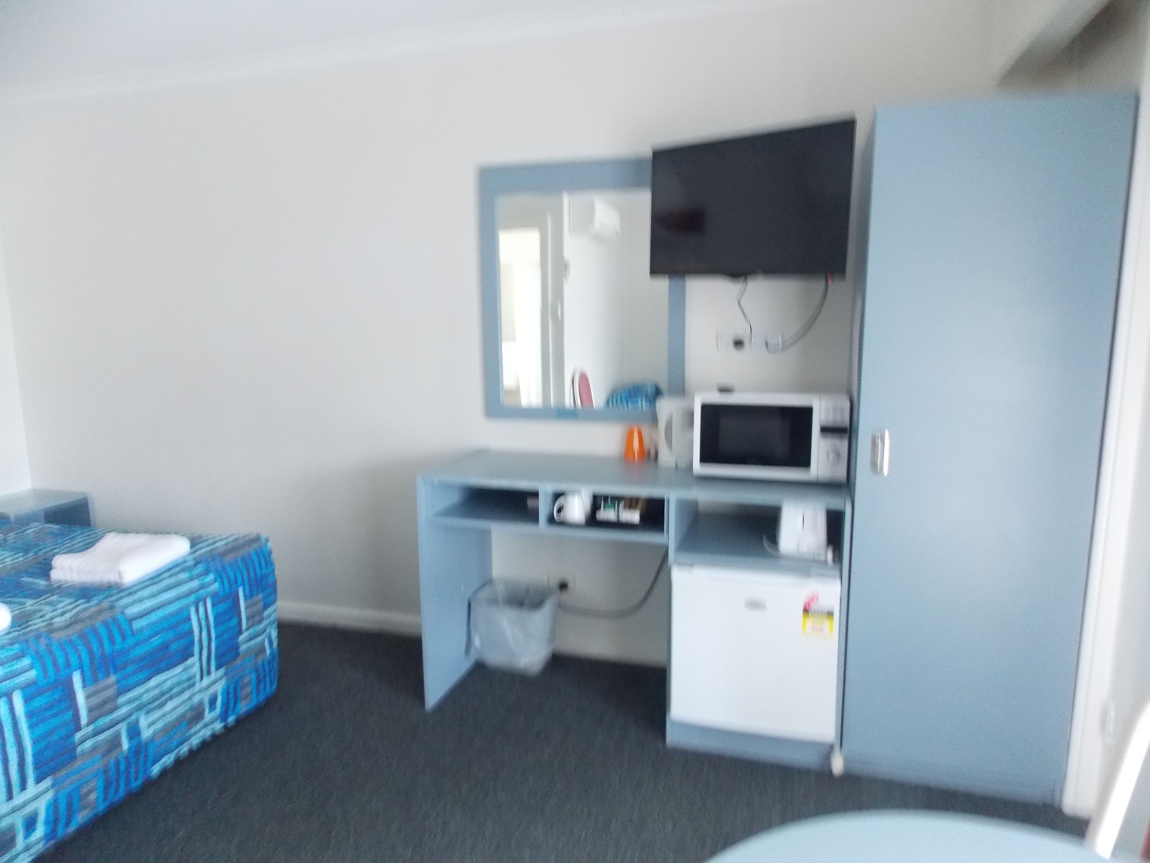 Una habitación compacta con cama, escritorio con televisor, microondas y un mueble pequeño.