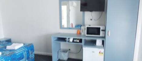Una habitación compacta con cama, escritorio con televisor, microondas y un mueble pequeño.